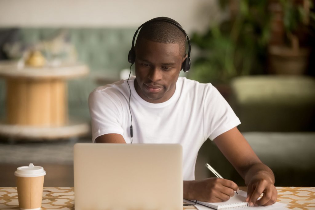man wearing headphones watching webinar making notes study online
