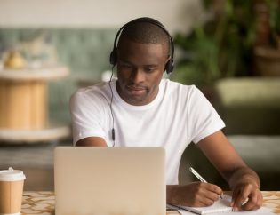 man wearing headphones watching webinar making notes study online