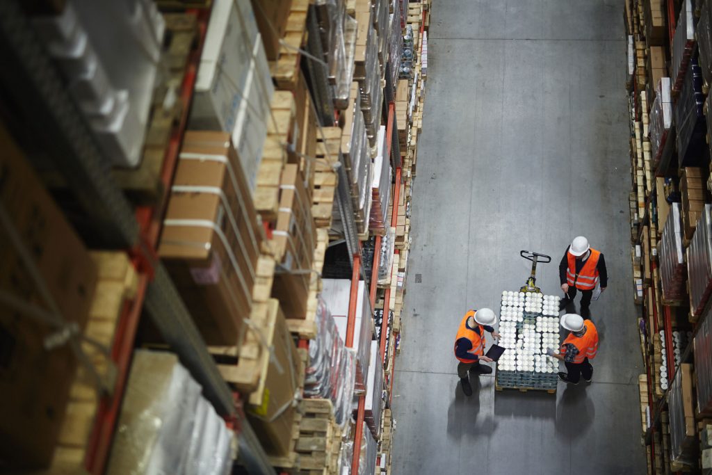 Above view of people working in large warehouse, counting goods on moving cart between shelves with packed boxes