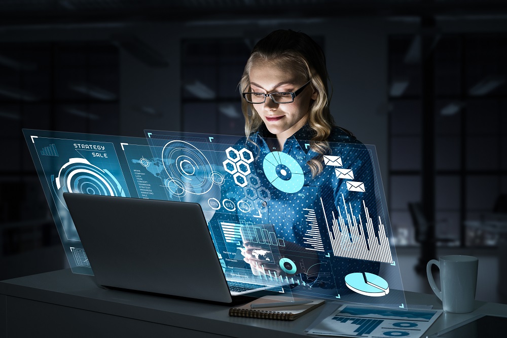 Attractive woman looking at her laptop screen sitting in night office. Mixed media