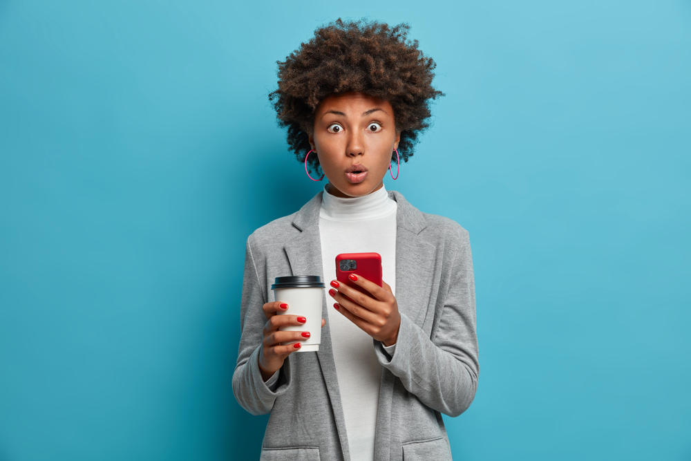 Woman with natural hair holding cell phone in surprise