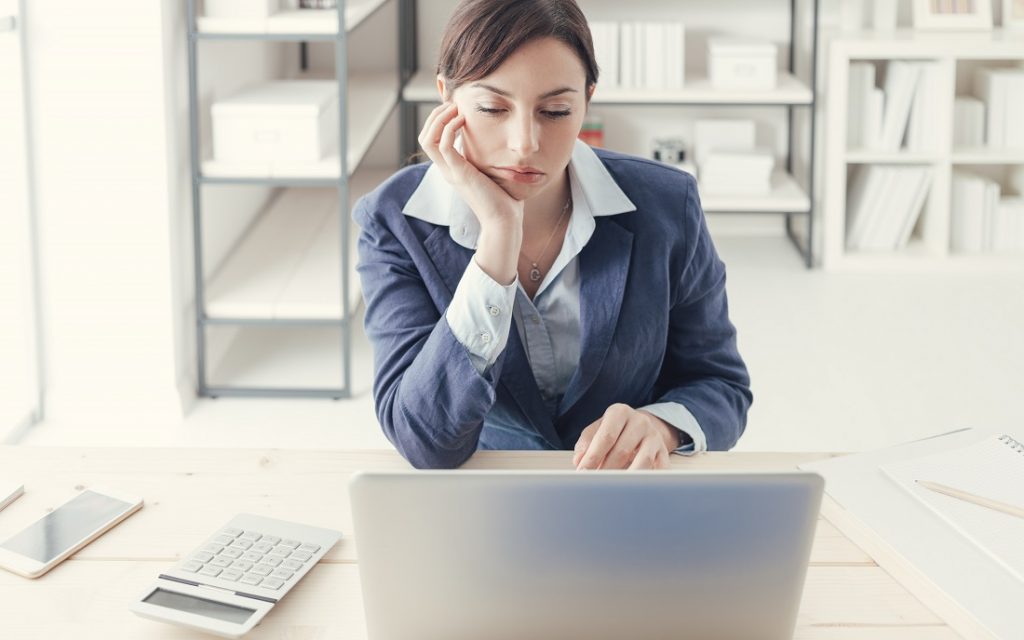 Depressed bored businesswoman working at office desk and networking with a laptop, boring job concept