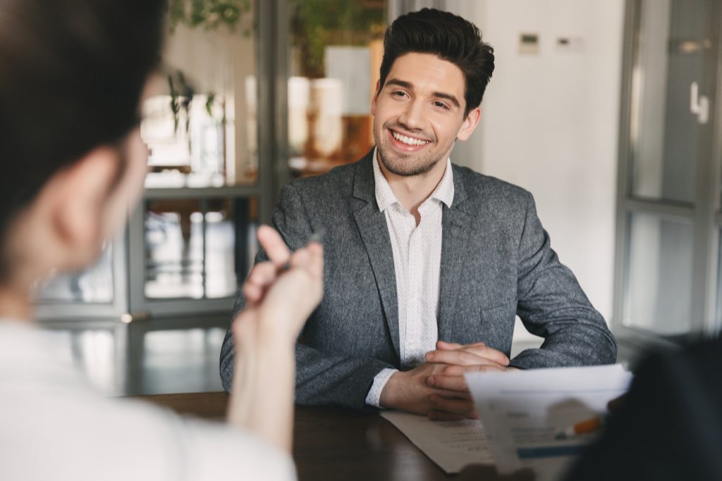 Business, career and placement concept - smiling caucasian man 30s negotiating with committee of businesslike people during job interview in office